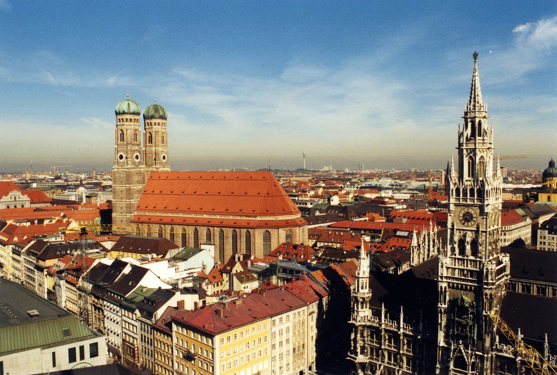 Blick über die Dächer Münchens mit den Türmen der Frauenkirche und der Alpenkette am Horizont