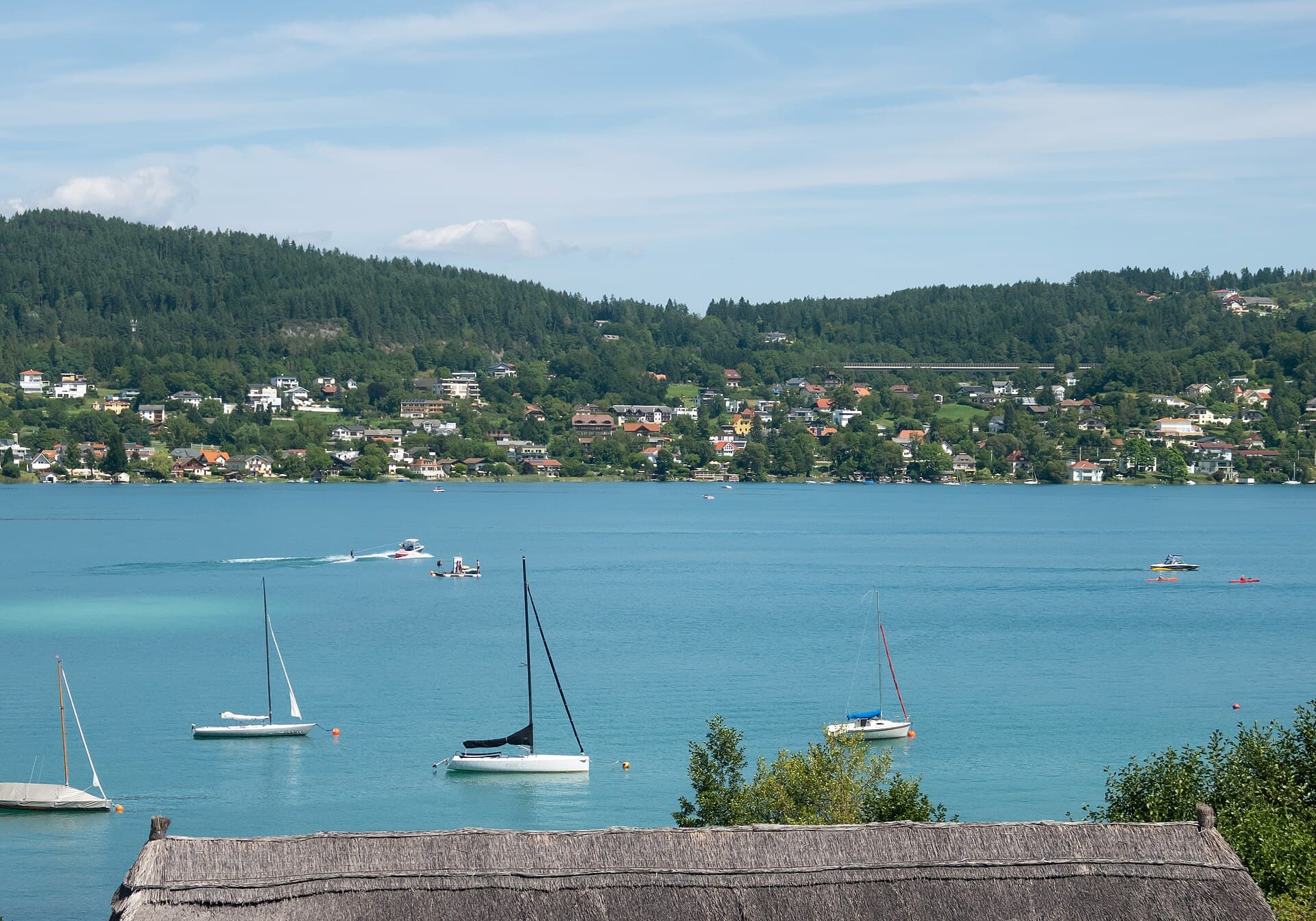 Blick über den Wörthersee auf Pörtschach in Kärnten mit Uferzone, Villen und bewaldeten Höhen im Hintergrund